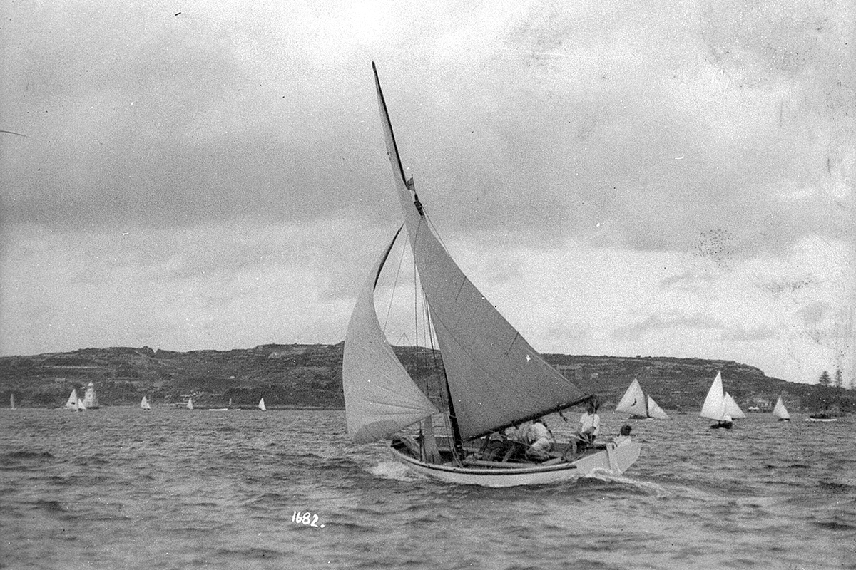 A couta type yacht sailing north on Sydney Harbour with South Head and Watson's Bay in distance. ANMM Collection 00011020. William James Hall.