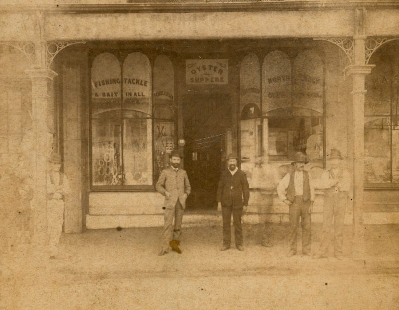 Photograph of three men standing outside a shop in George Street during the 1880s