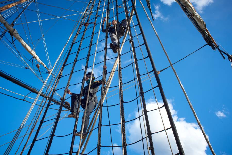 Two people climbing rigging on a ship