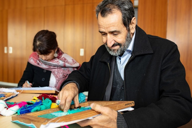 Artists Sayd Abdali (right) and Jane Théau worked to make a tapestry rug at the museum during Refugee Week whose design celebrates the new lives that refugees begin in Australia