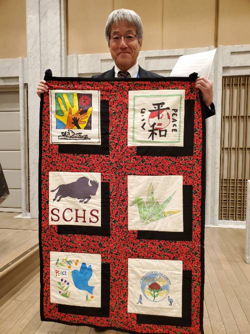 Deputy Director of the Hiroshima Peace Memorial Museum, Katsunobu Hamaoka, with a quilt made and donated by the students participating in the education program. Image David Foley