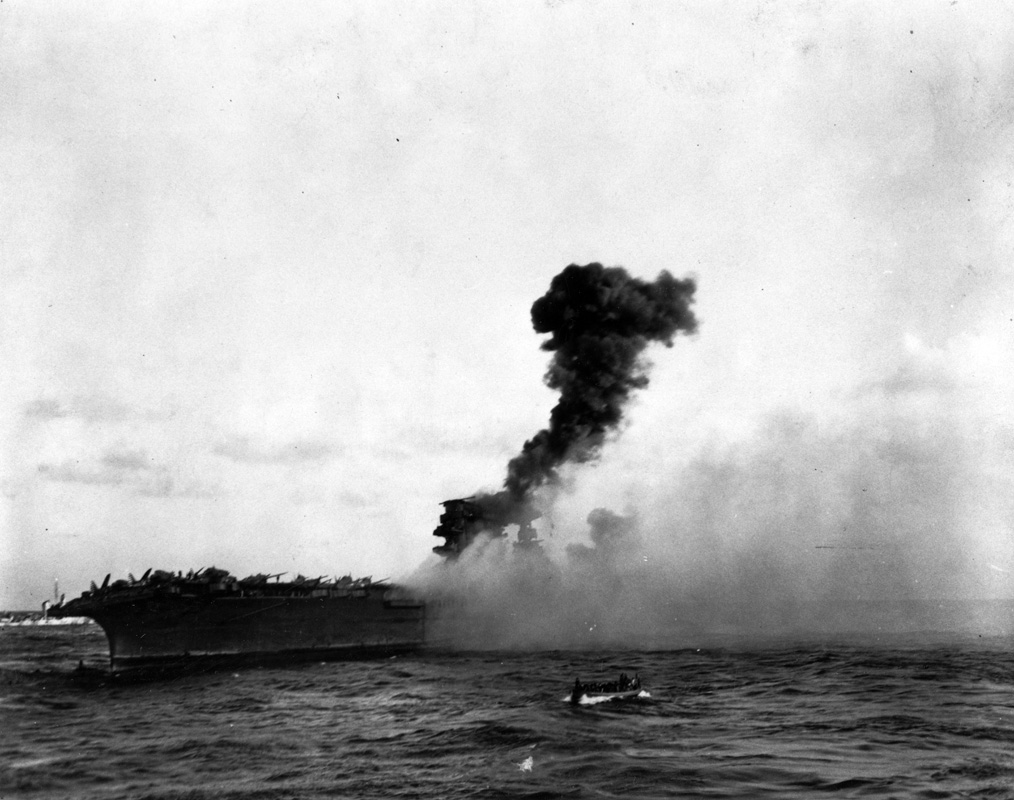 An explosion amidships on USS <em>Lexington</em> (CV-2), while it was being abandoned during the afternoon of 8 May 1942. This may be the explosion reported to have taken place at 17:27 hrs, which was followed by a great explosion aft as stowed torpedo warheads detonated on the hangar deck. Note whaleboat underway in the foreground. Image: Official US Navy photograph collection of the National Archives, Naval History and Heritage Command BD-G-7406.