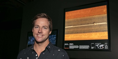 Photojournalist Justin Gilligan standing in front of his photograph, Colliding Views