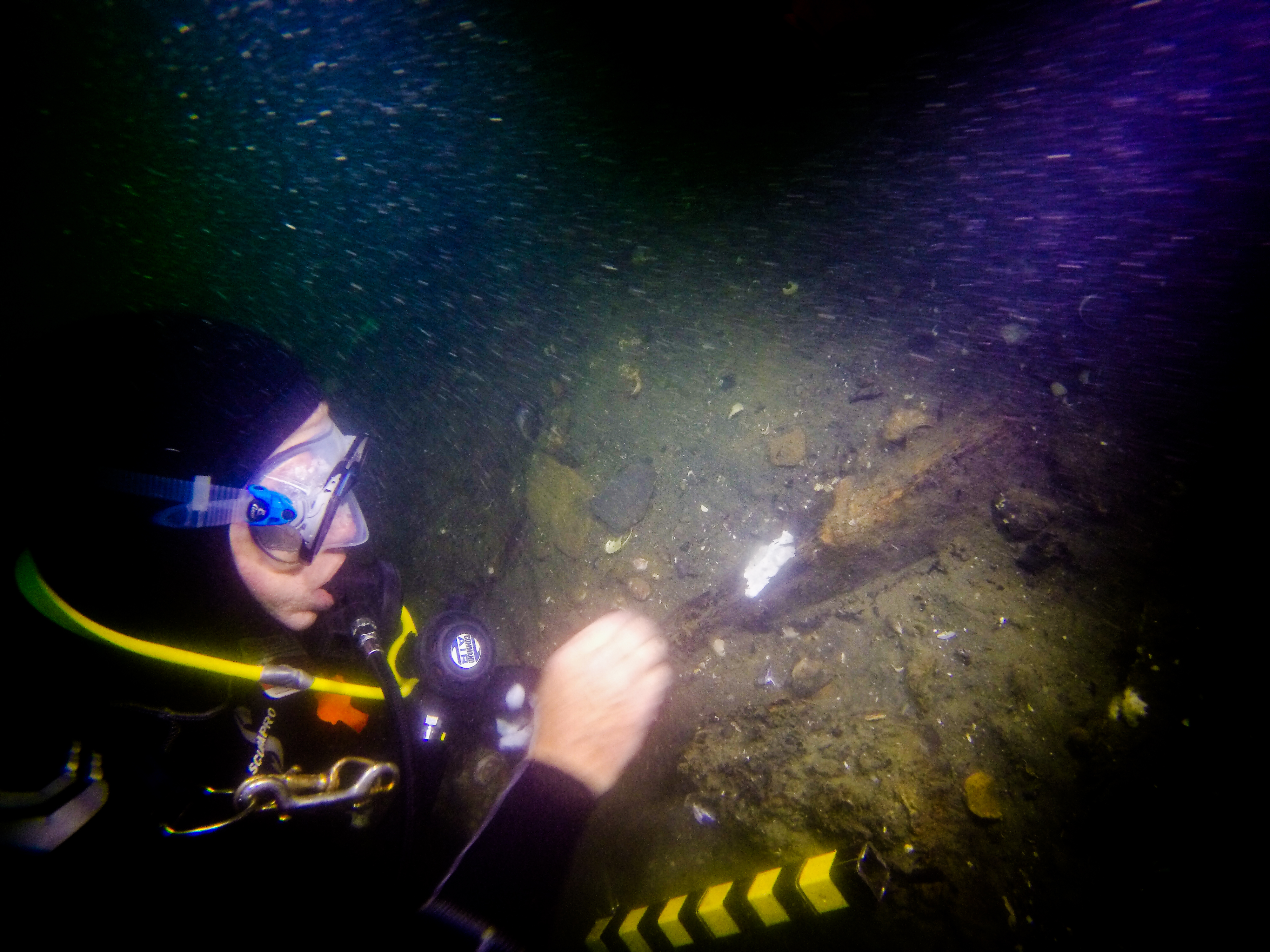 A diver working on the seafloor with a light, examining part of a wreck 